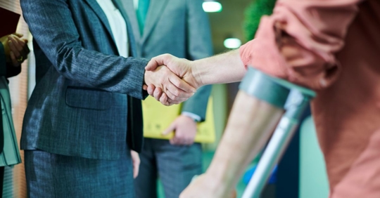 man using a walking support device shaking hands with a woman wearing a business suit