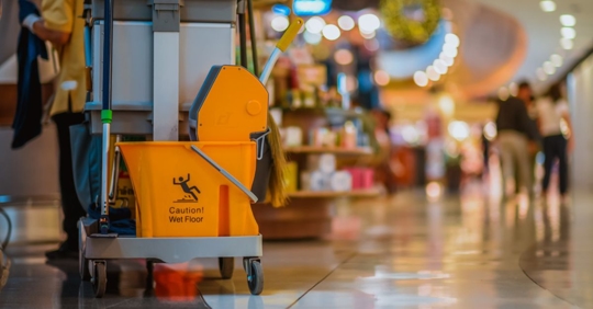 a close up of a janitor cart with a mop bucket being pushed through a retail center