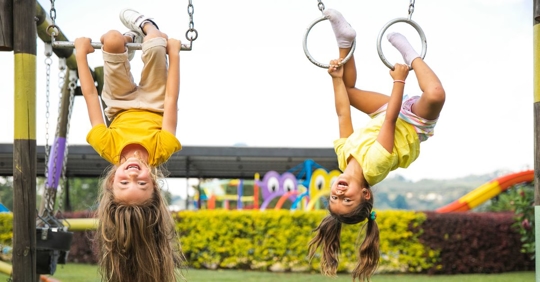 two young girls hanging upside down on playground equipment