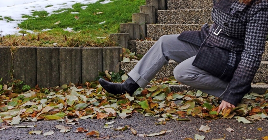 close up of a woman wearing boots and trench coat falling down the stairs on top of a pile of fall leaves